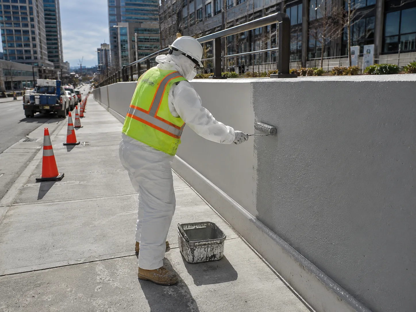 Representative protected painter rolling an exterior wall beside a downtown city street